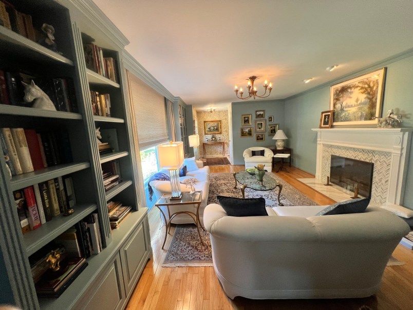 A cozy living room featuring a white sofa, a glass coffee table, and a bookshelf filled with books, illuminated by soft lighting and decorated with artwork on the walls.